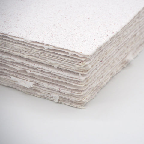 A stack of white deckle edge hand made paper embedded with red glitter
