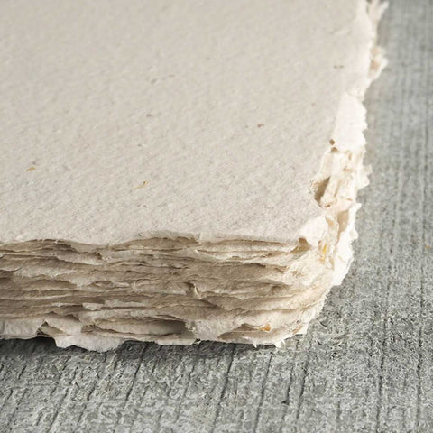 A stack of off-white deckle edge hand made paper embedded with spent grains