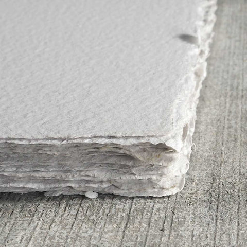A stack of light gray deckle edge hand made paper with flecks of ink throughout 