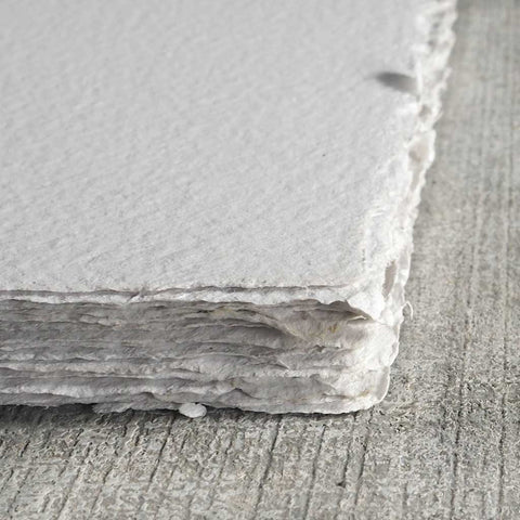 A stack of light gray deckle edge hand made paper with flecks of ink throughout