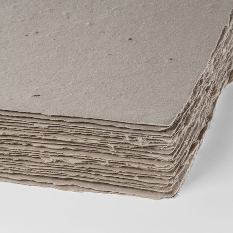 A stack of mushroom brown deckle edge hand made paper embedded with wildflower seeds