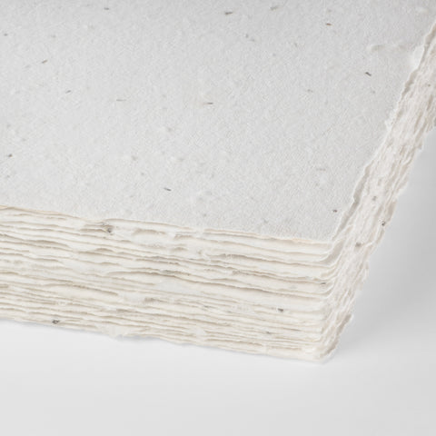 A stack of natural white deckle edge handmade paper embedded with wildflower seeds