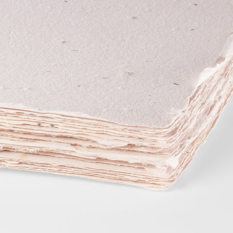 A stack of blush pink deckle edge hand made paper embedded with wildflower seeds