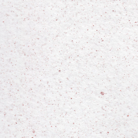 A closeup of white deckle edge hand made paper embedded with red glitter