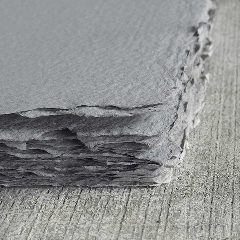 A stack of charcoal gray deckle edge hand made paper made with 100% recycled wood fiber