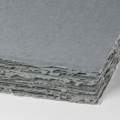 A stack of dusty blue deckle edge hand made paper embedded with wildflower seeds